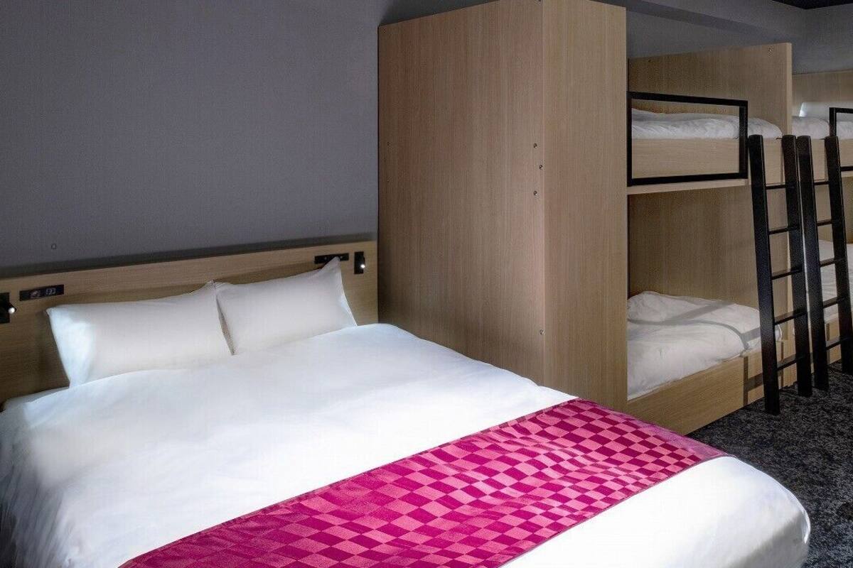 A hotel room with a single bed, a bunk bed, a desk, and a chair.