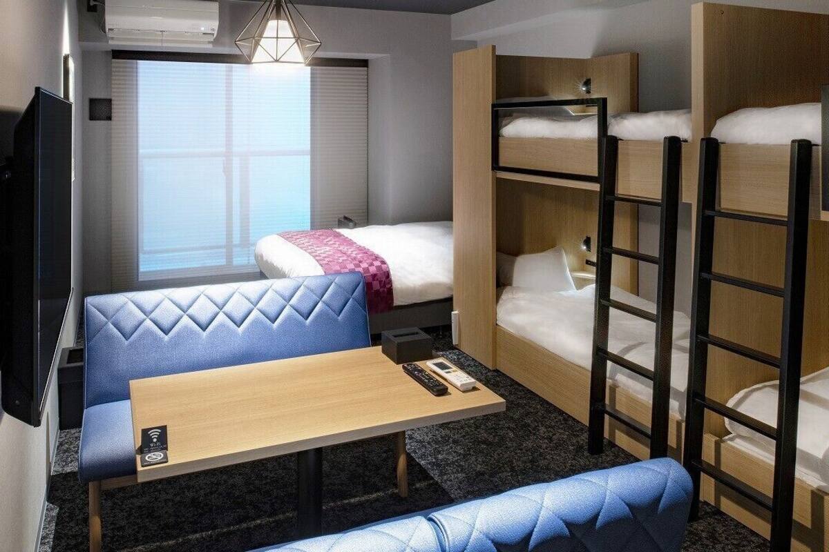 A compact room with bunk beds, a sofa, a small table, a TV, and an air conditioning unit.