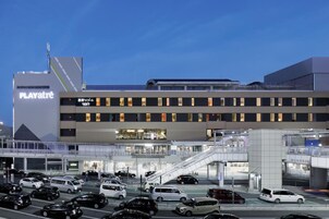 A multi-story building with a prominent 'PLAYatre' sign, a covered pedestrian walkway, and a parking area with various vehicles.
