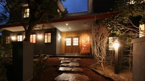 A modern building with a stone pathway leading to a wooden door, surrounded by trees and illuminated by ambient lighting. - Izukogen Onsen Kura no Yado Hinata (Ito)