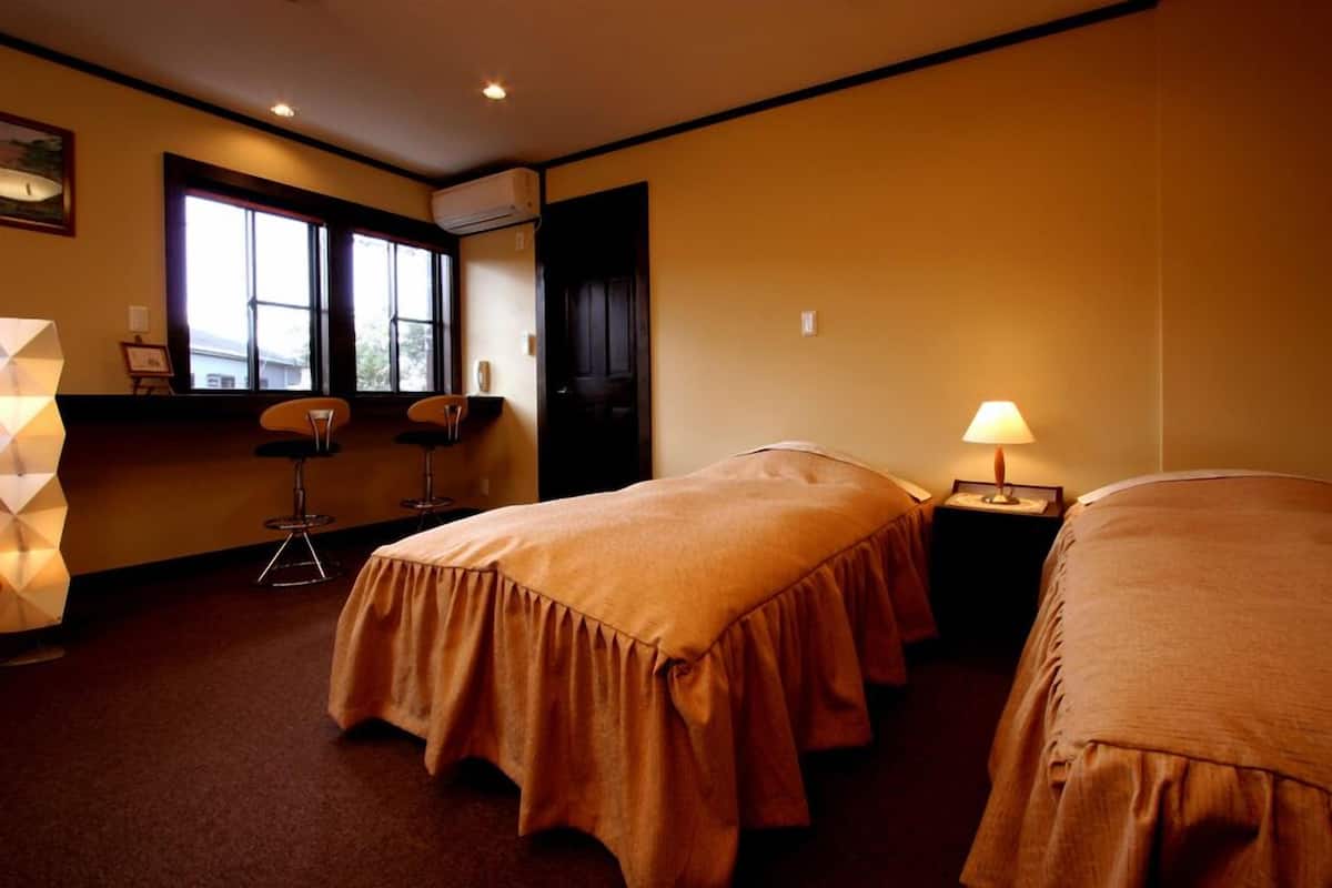 A hotel room with two beds, a window, a desk, and a chair.