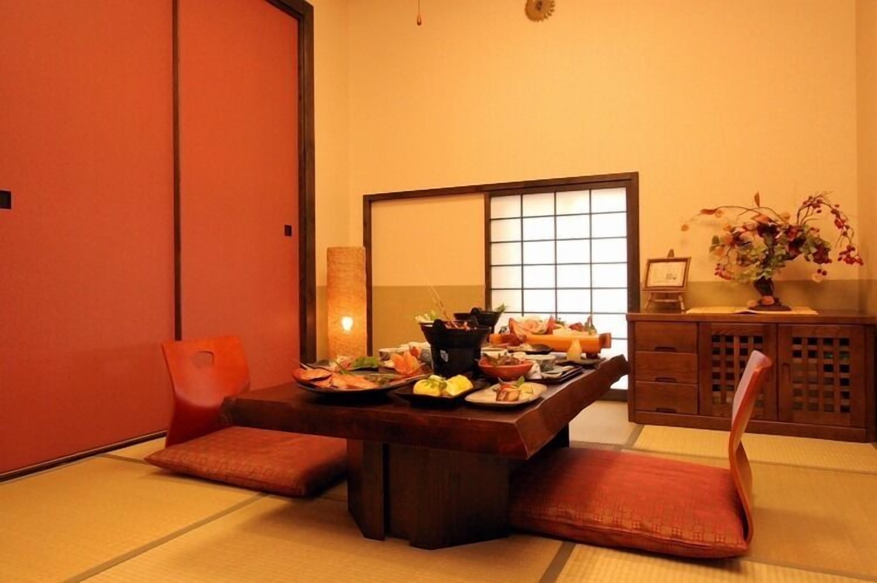Ein traditioneller japanischer Raum mit Tatami-Böden, einem niedrigen Tisch mit verschiedenen Speisen und einer Holzkassette mit einem Blumenstrauß.