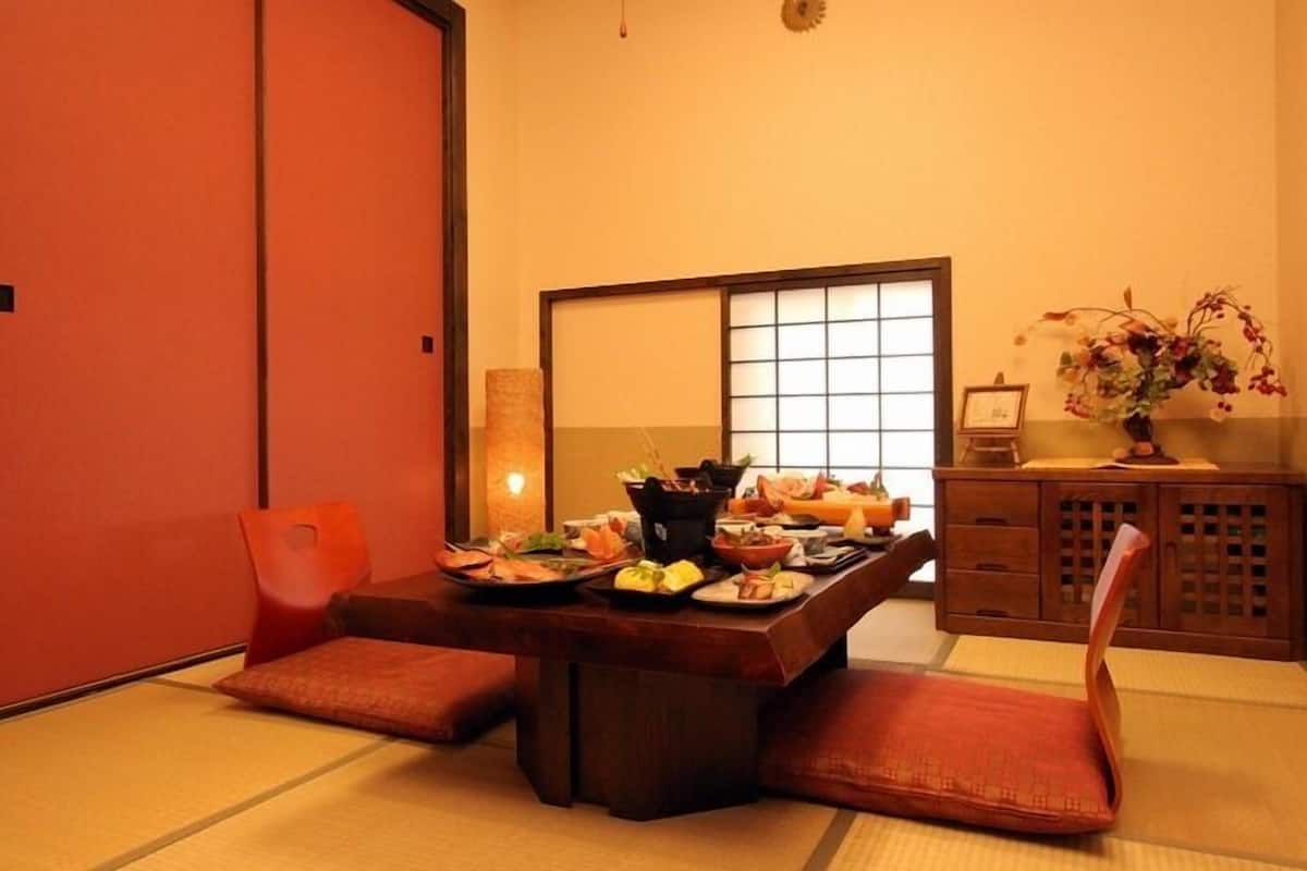 A traditional Japanese room with tatami flooring, a low table with a variety of dishes, and a wooden cabinet with a vase of flowers.