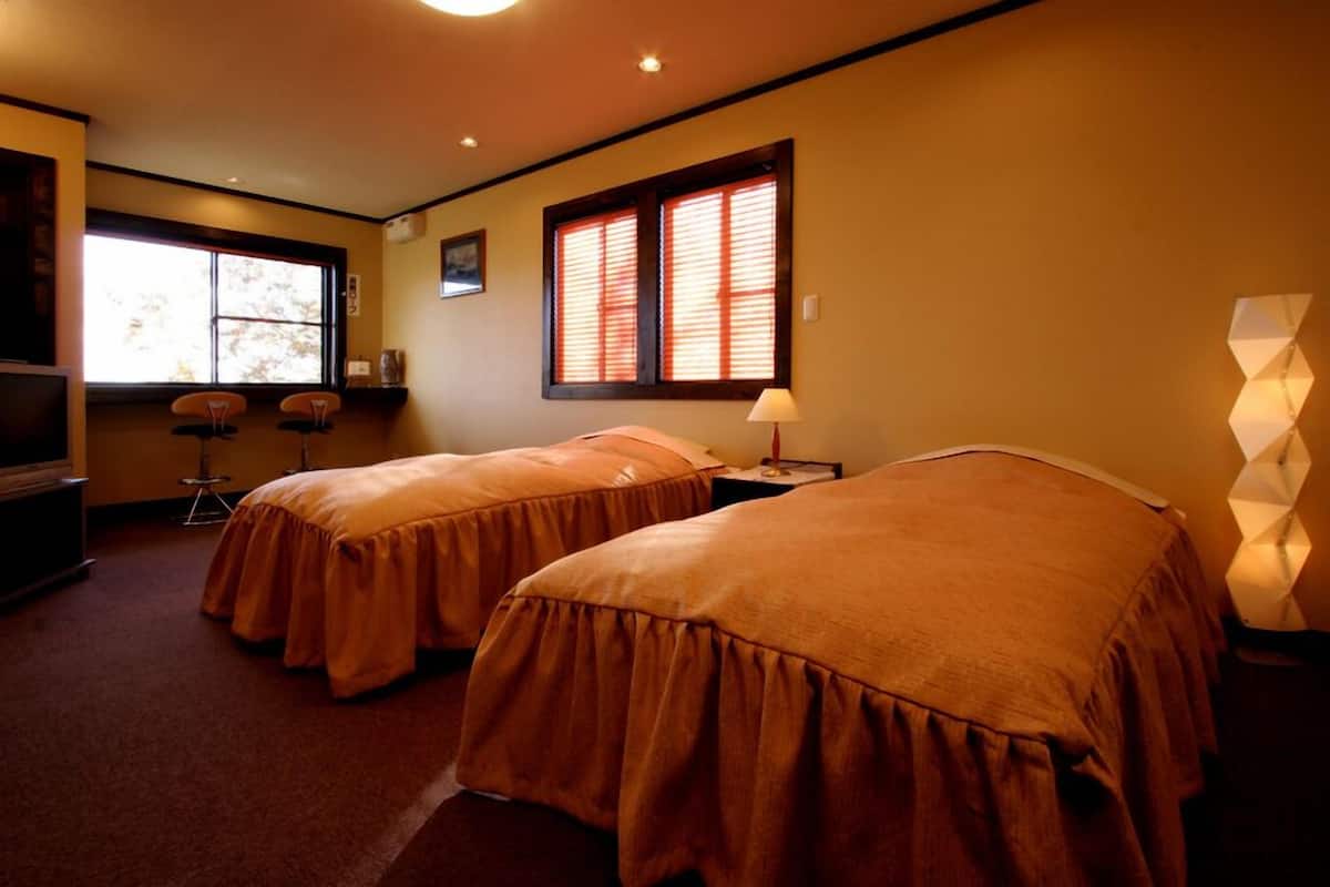 A hotel room with two beds, a TV, a window with blinds, and a lamp.