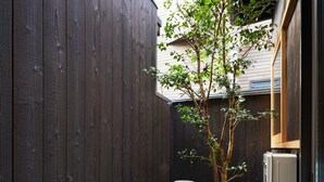 Un cortile stretto con una recinzione in legno, un piccolo albero, una lanterna in pietra e un frigorifero.