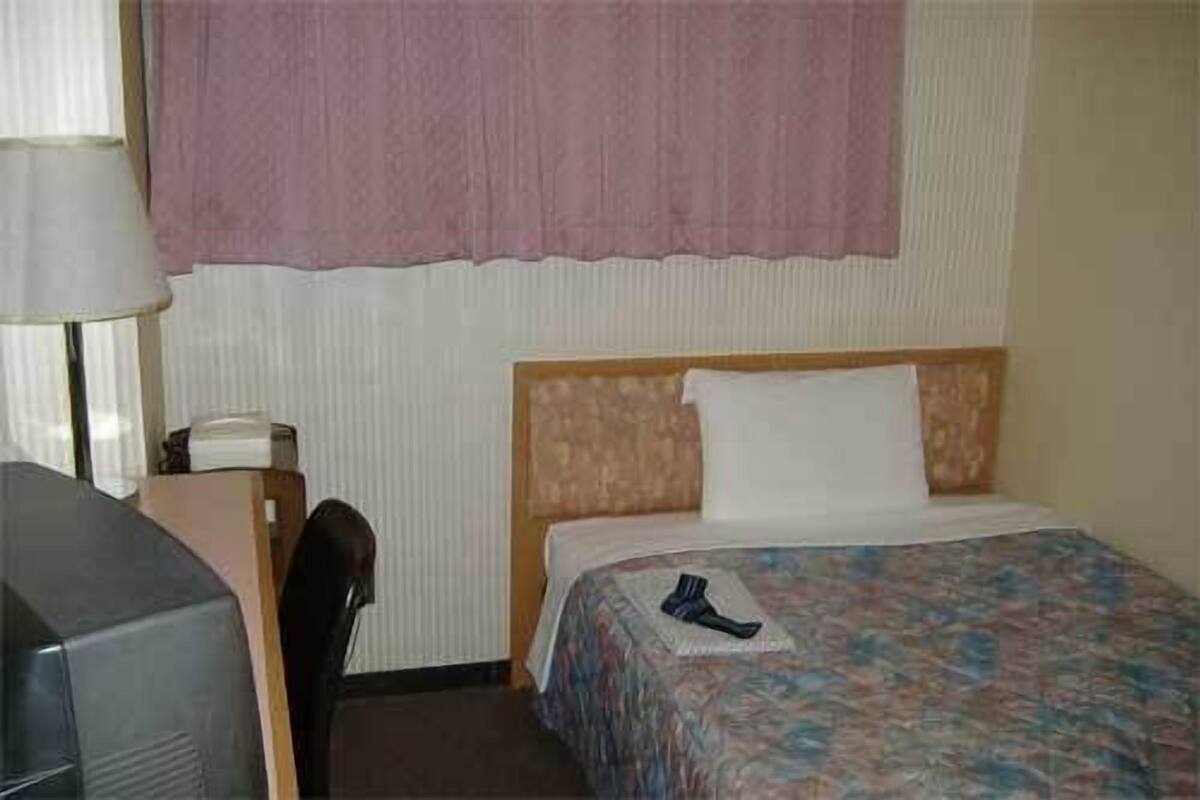 A hotel room with a bed, a desk with a telephone, and a chair.