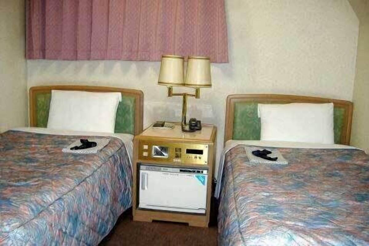 A hotel room with two beds, a nightstand with a lamp, and a small refrigerator.