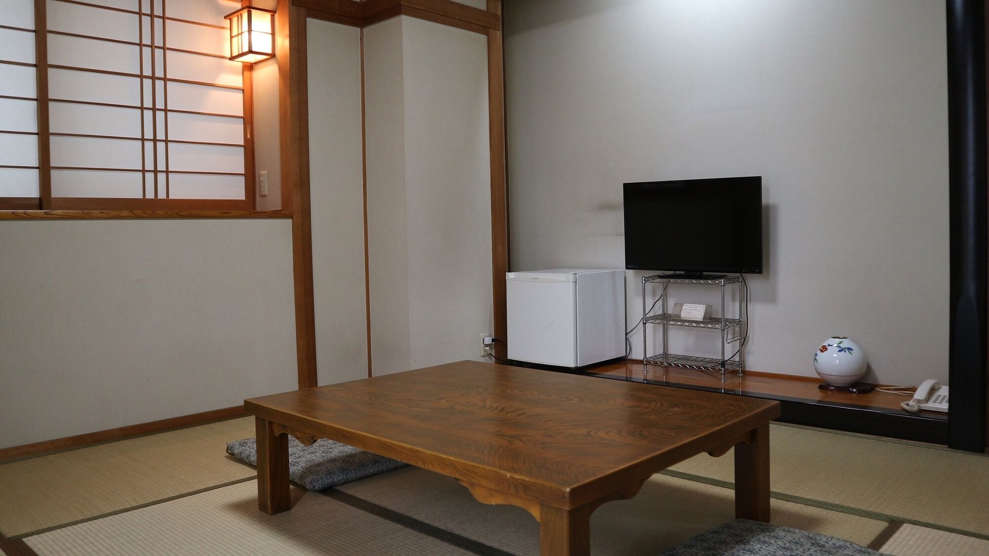 A traditional Japanese room with tatami flooring, a wooden table, a television on a stand, and a small white appliance.