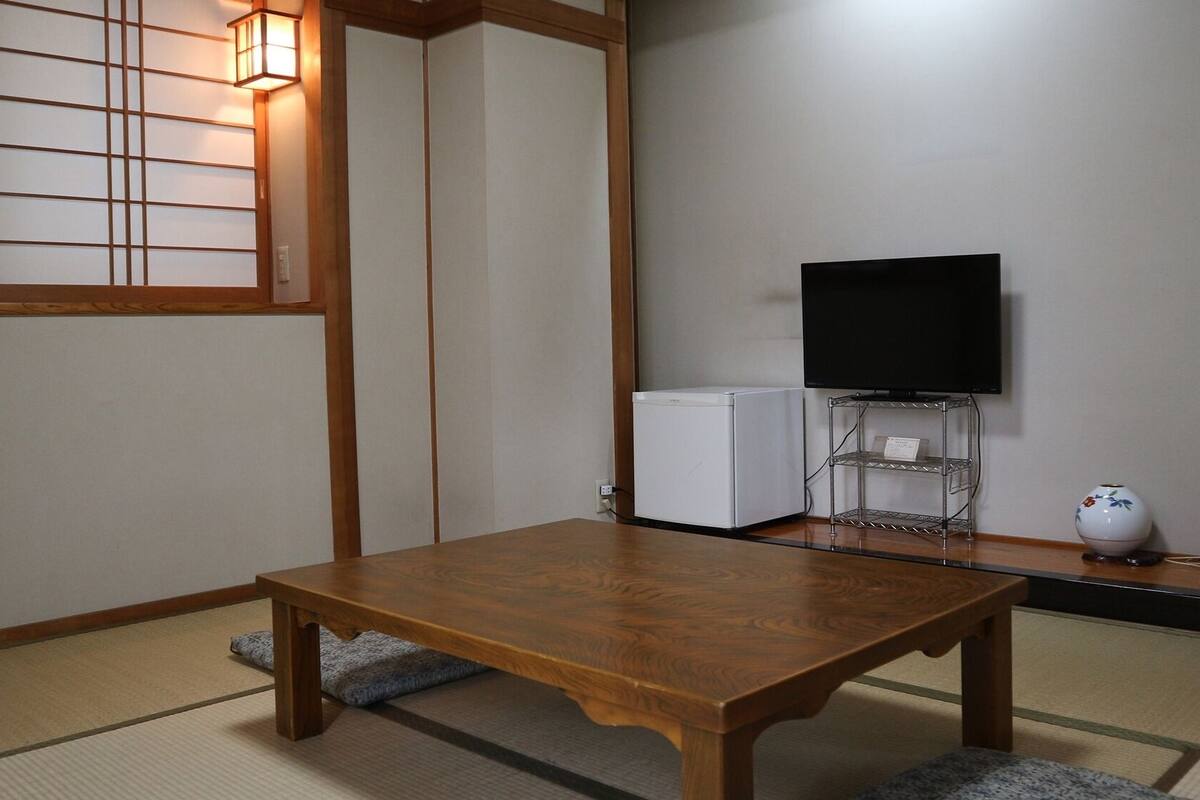 A traditional Japanese room with tatami flooring, a wooden table, a television on a stand, and a small white appliance.