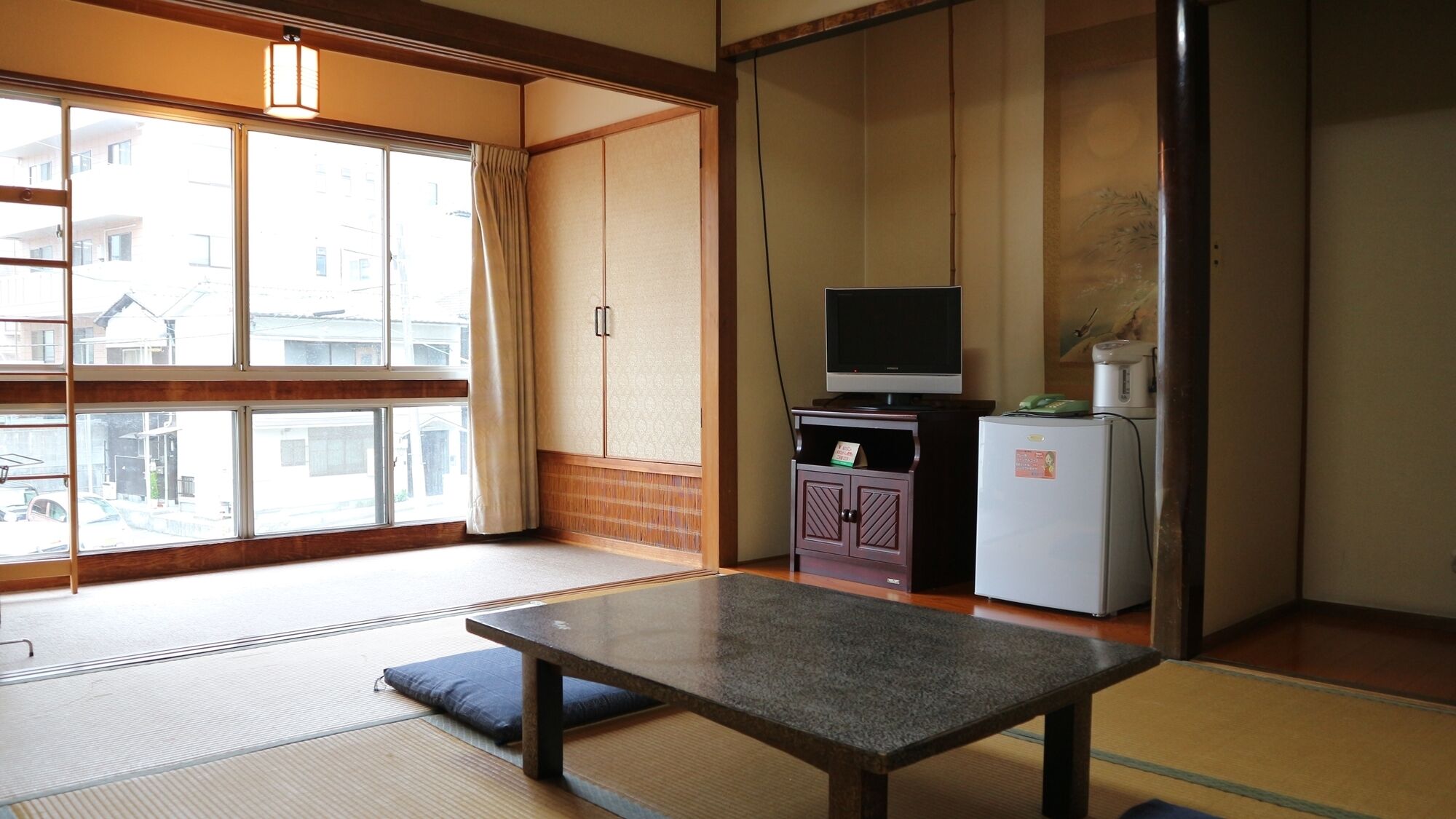 A traditional Japanese room with tatami flooring, a low table, a television, and a refrigerator.