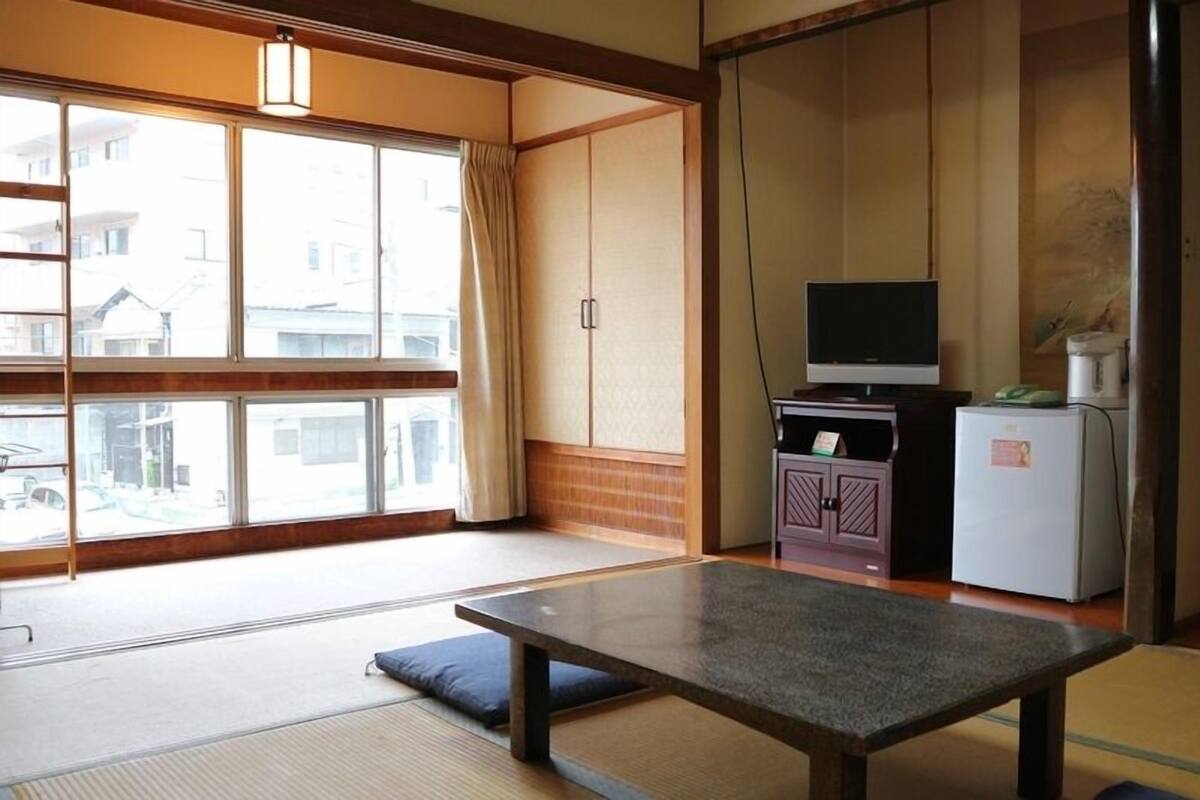 A traditional Japanese room with tatami flooring, a low table, a television, and a refrigerator.