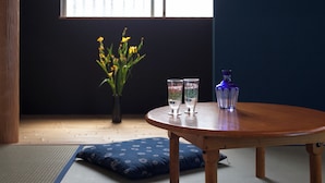 Une pièce avec un sol recouvert de tatamis, une table en bois, un vase contenant des fleurs jaunes, deux verres et un vase bleu.