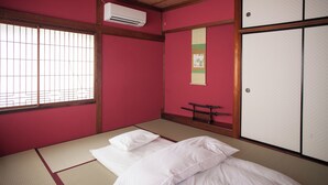 Une pièce de style japonais traditionnel, avec un sol recouvert de tatamis, un futon servant de lit, des portes coulissantes et un appareil de climatisation.