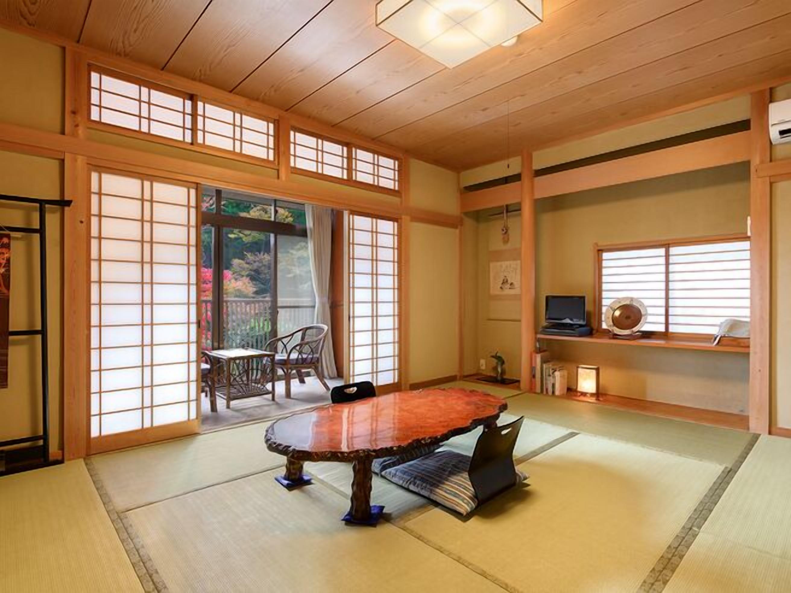 A traditional Japanese room with tatami flooring, a low table, sliding doors, and a television on a shelf.