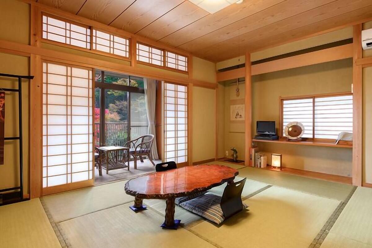 Una habitación japonesa tradicional con suelo de tatami, una mesa baja, puertas correderas y un televisor sobre una estantería.