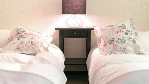 Une chambre avec deux lits, chacun agrémenté de draps à motifs floraux, une table de chevet avec une lampe et un mur décoré d’un motif.