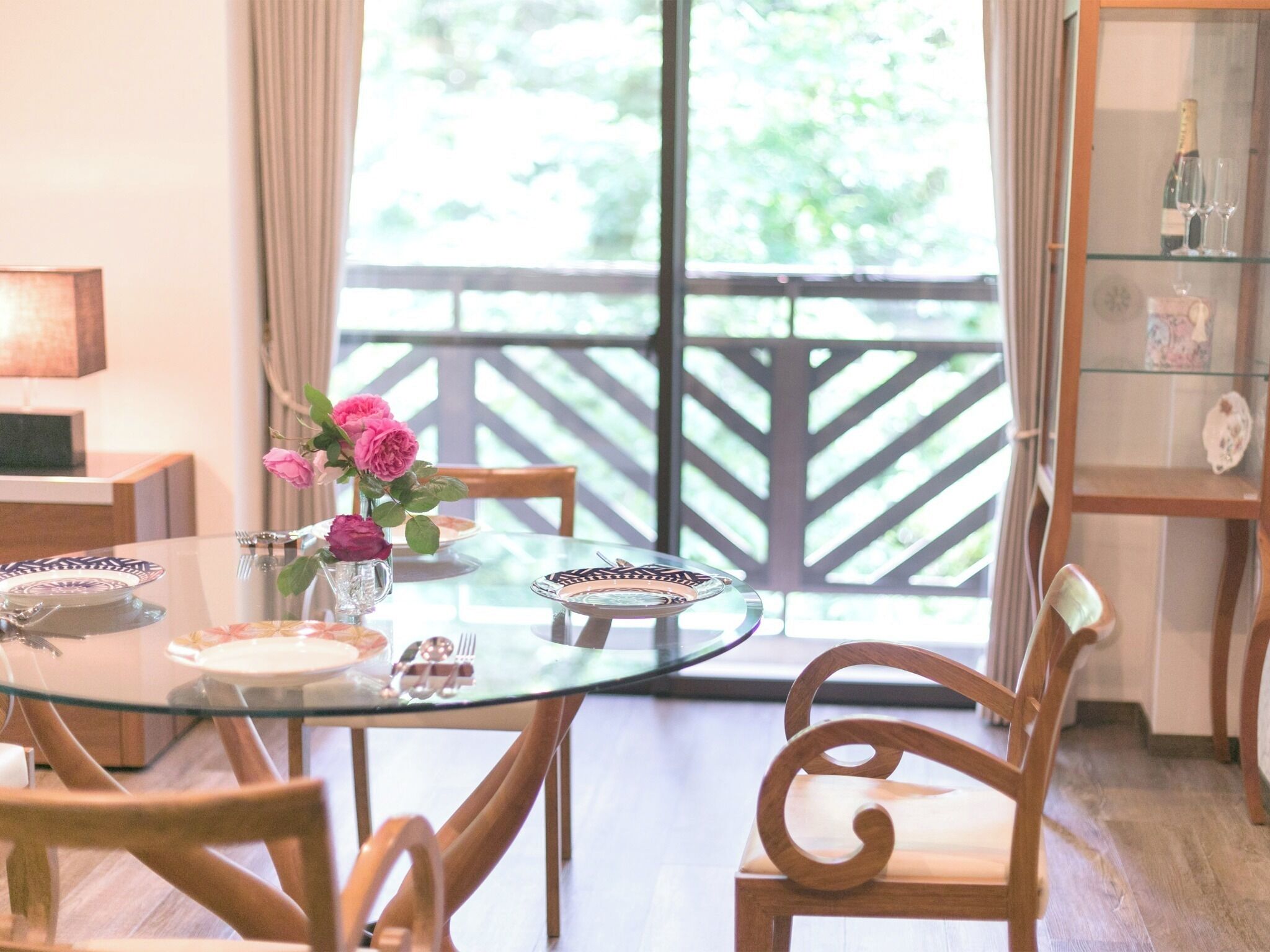 A dining area with a glass table, wooden chairs, and a vase of flowers.