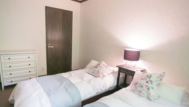 Une chambre avec deux lits, une commode, une porte et une table de chevet avec une lampe.