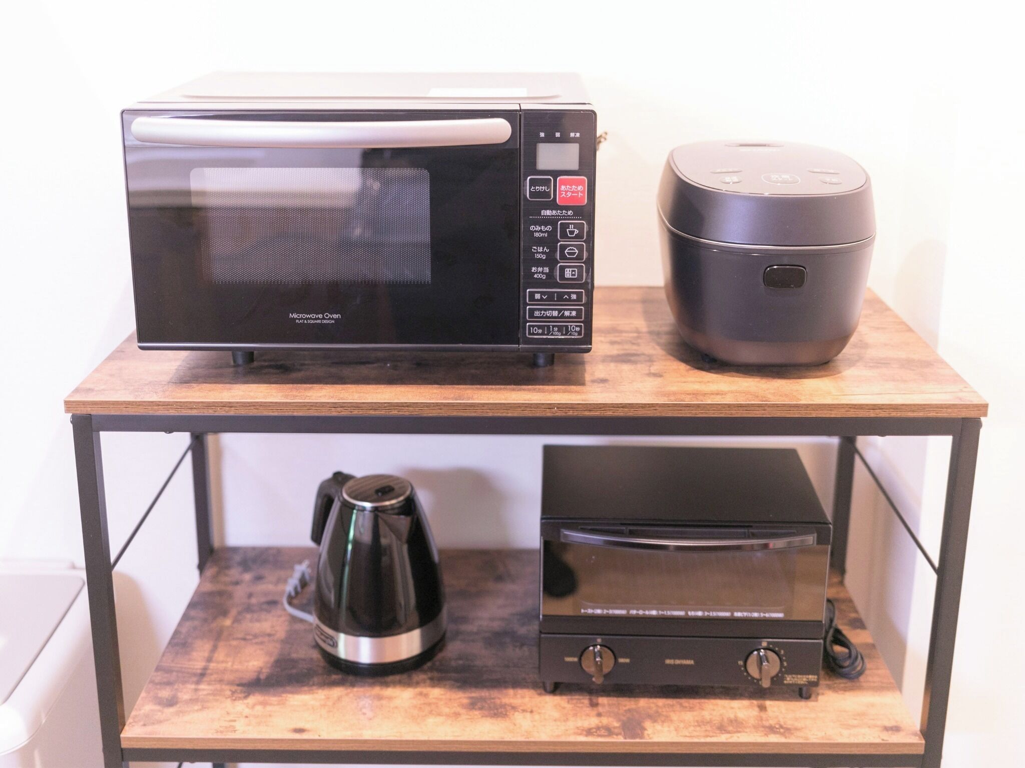A microwave oven, a rice cooker, and a coffee maker on a wooden table.