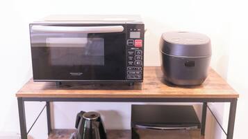 A microwave oven, a rice cooker, and a coffee maker on a wooden table.