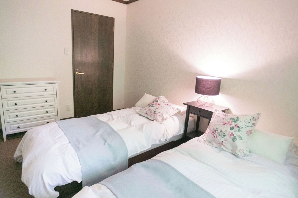 Une chambre avec deux lits, une commode, une porte et une table de chevet avec une lampe.
