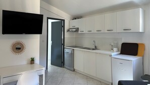 A compact kitchen with white cabinets, a built-in dishwasher, and a flat-screen TV mounted above the counter. - Prestige Relax, private Bastidons and exclusive setting on 4 hectares with swimming pool (Fréjus)