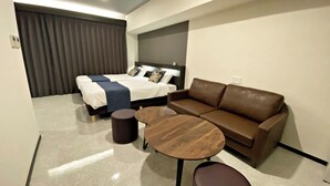 Una habitación de hotel moderna con una cama, un sofá de cuero marrón, una mesa de centro de madera y una pequeña mesa redonda.