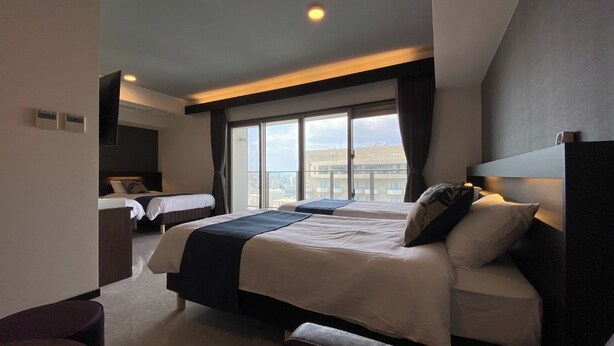 Habitación de hotel moderna con dos camas, un ventanal amplio con vistas a la ciudad y una zona de estar separada.