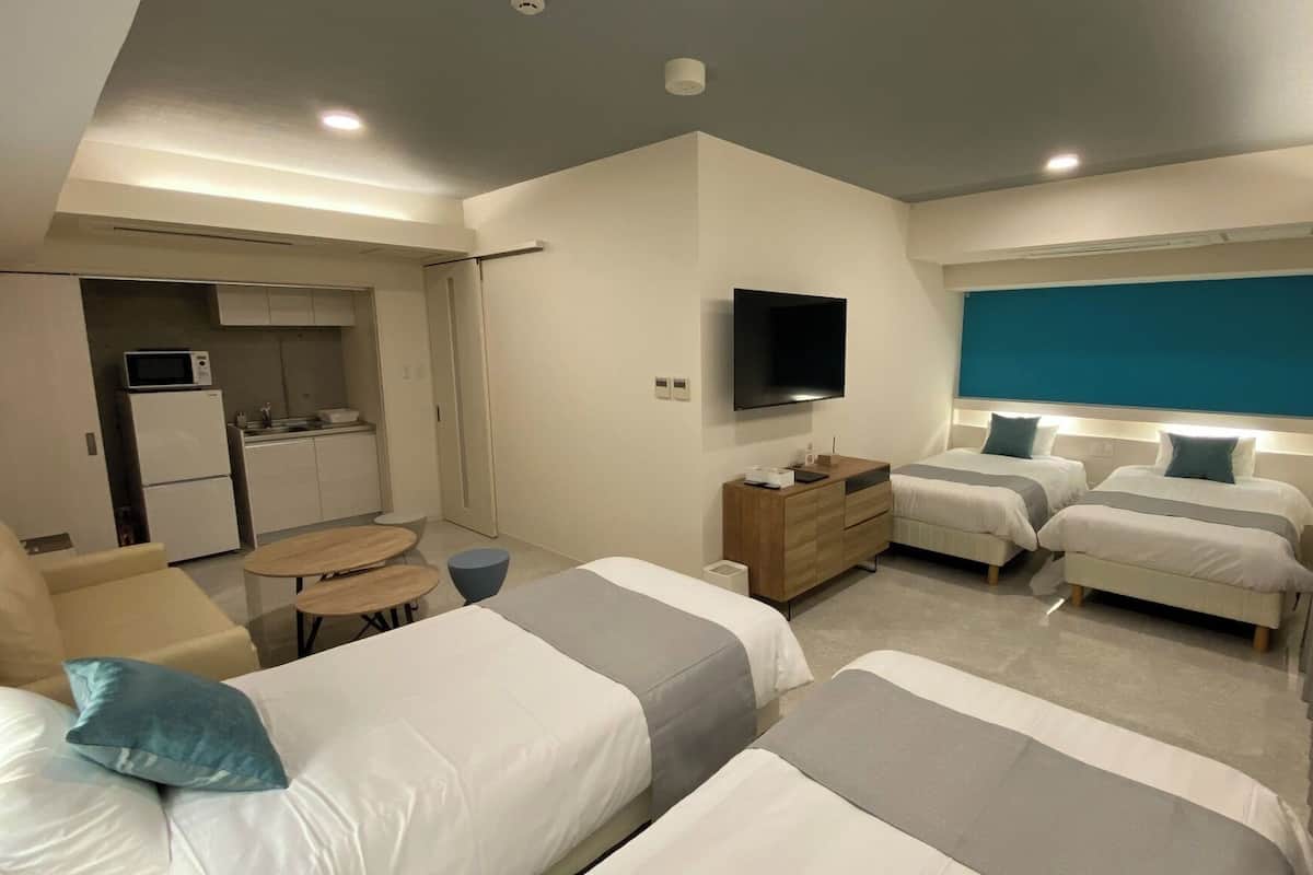 A modern hotel room with two beds, a TV, a small kitchenette, and a seating area.