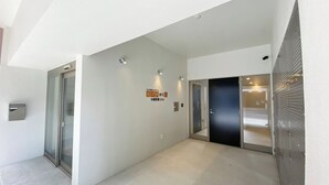 Un pasillo moderno con puertas de vidrio, un cartel que indica una habitación en el segundo piso y una barandilla de metal a la derecha.