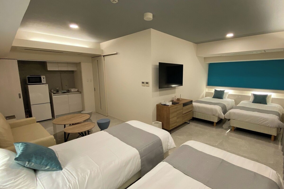 Une chambre d’hôtel moderne équipée de deux lits, d’une télévision, d’une petite kitchenette et d’un coin salon.