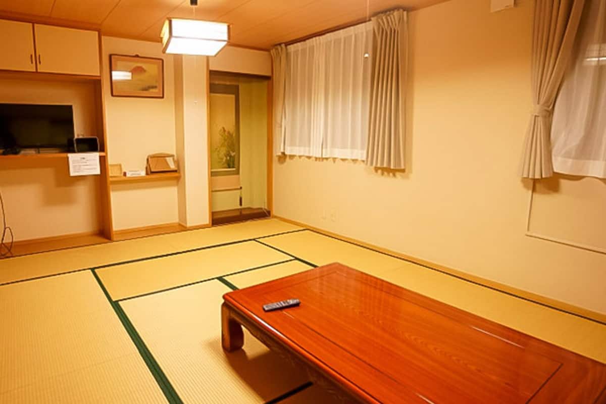 A traditional Japanese room with tatami flooring, a wooden table, a television, and a sliding door.