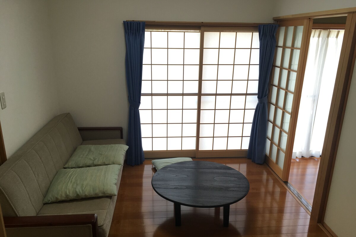 A room with a sofa, a round table, and a sliding glass door with blue curtains.