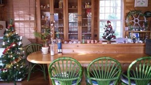 A dining area with a wooden table and green chairs, a Christmas tree, and a window with blinds. - Pension Schooner (Nasu)