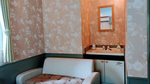 Un baño con papel tapiz floral, un espejo, un lavamanos con dispensador de jabón y un perchero para toallas.
