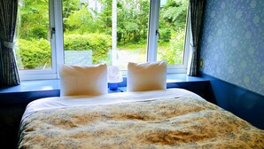 A bed with a floral bedspread, two pillows, and a view of a garden through a window. - Pension Schooner (Nasu)