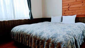 Un dormitorio con cabecera de madera, colcha estampada y ventana con cortinas.