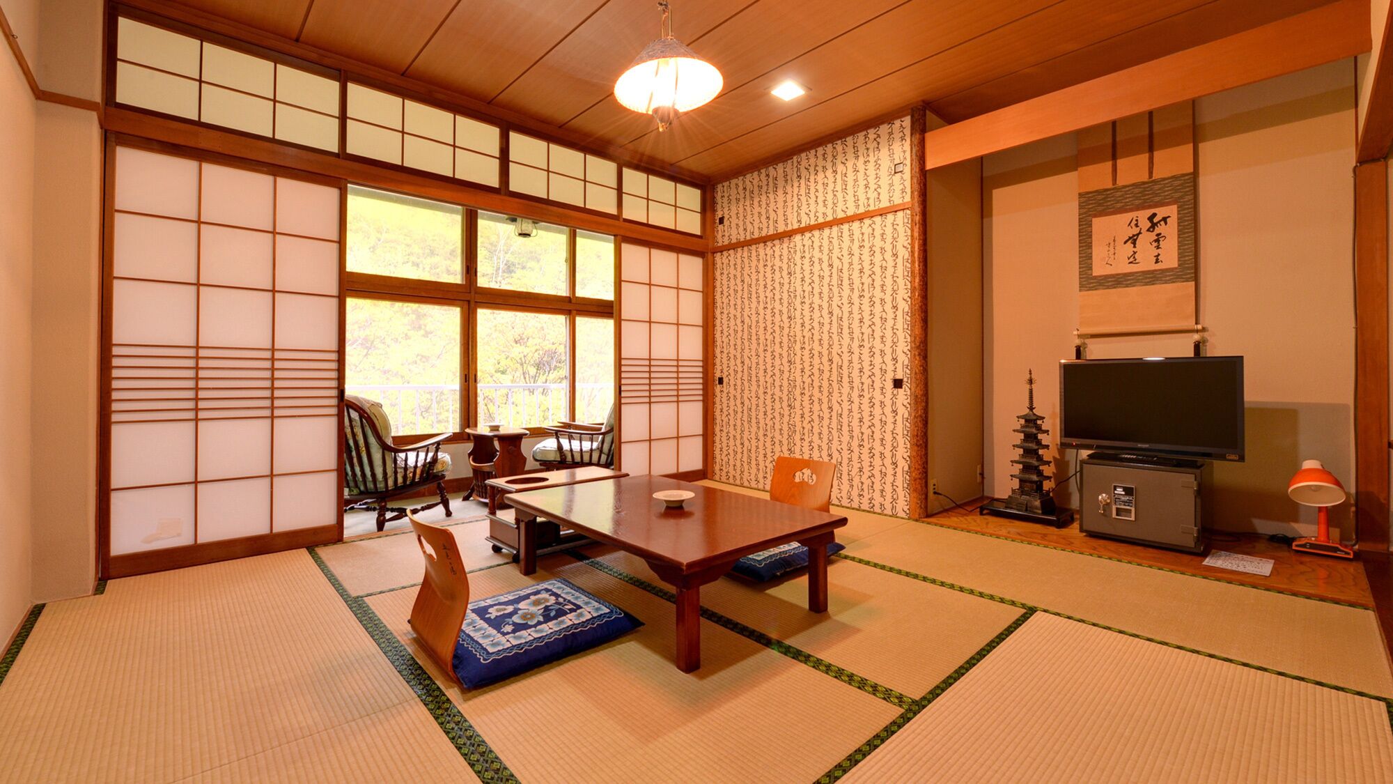 A traditional Japanese room with tatami flooring, a low table, a television, and a decorative shoji screen.
