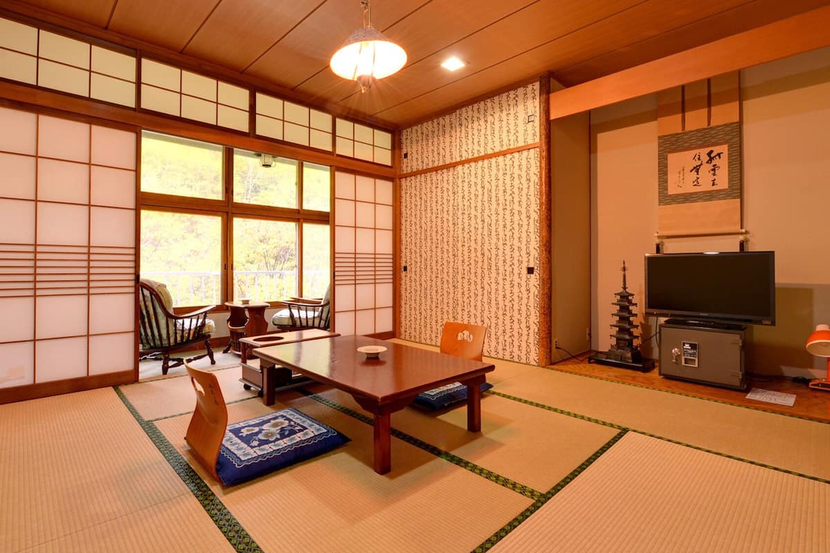 Ein traditioneller japanischer Raum mit Tatami-Böden, einem niedrigen Tisch, einem Fernseher und einem dekorativen Shoji-Bildschirm.