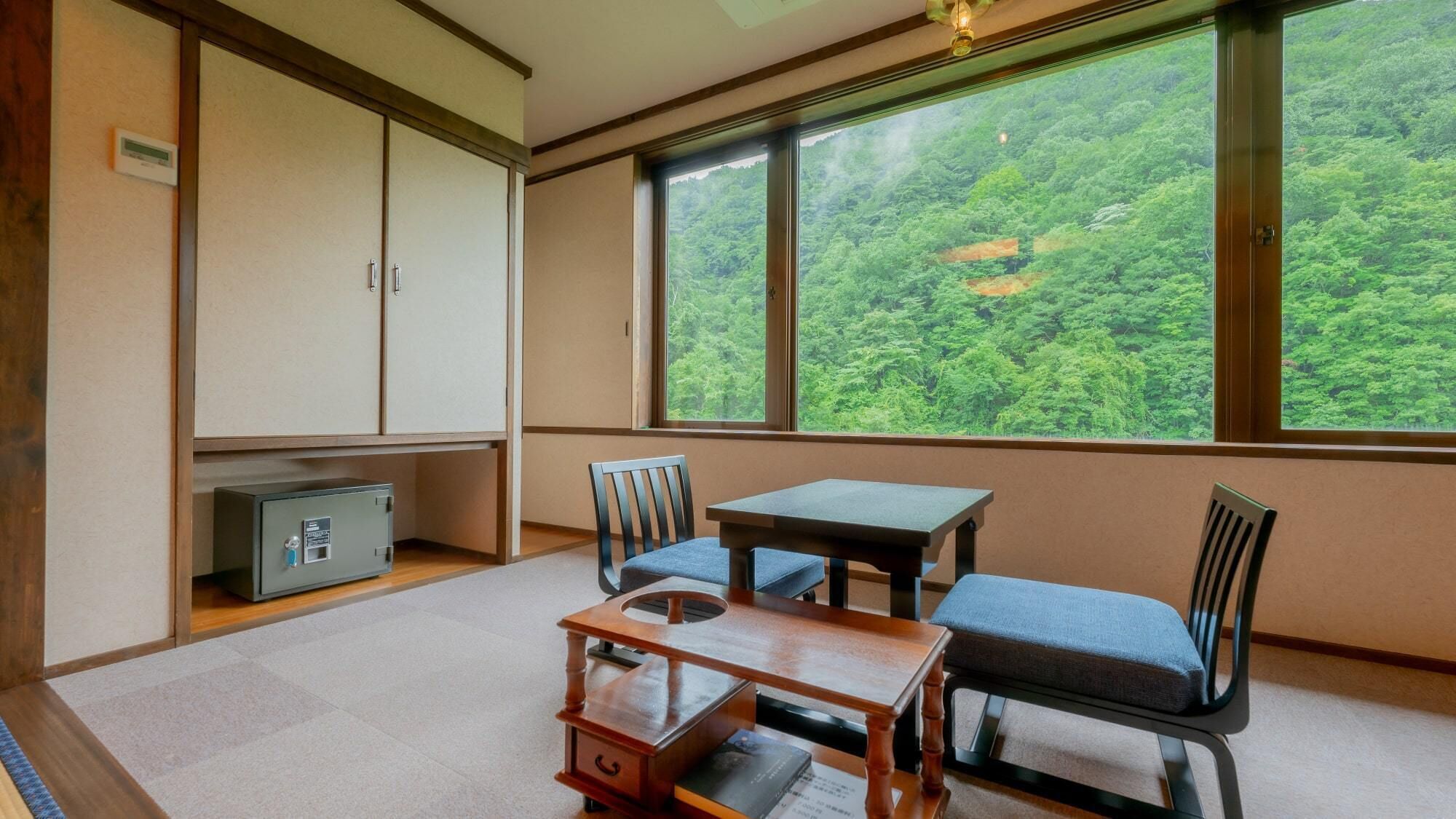 A room with a view of a forest, a small table, two chairs, a cabinet, and a safe.