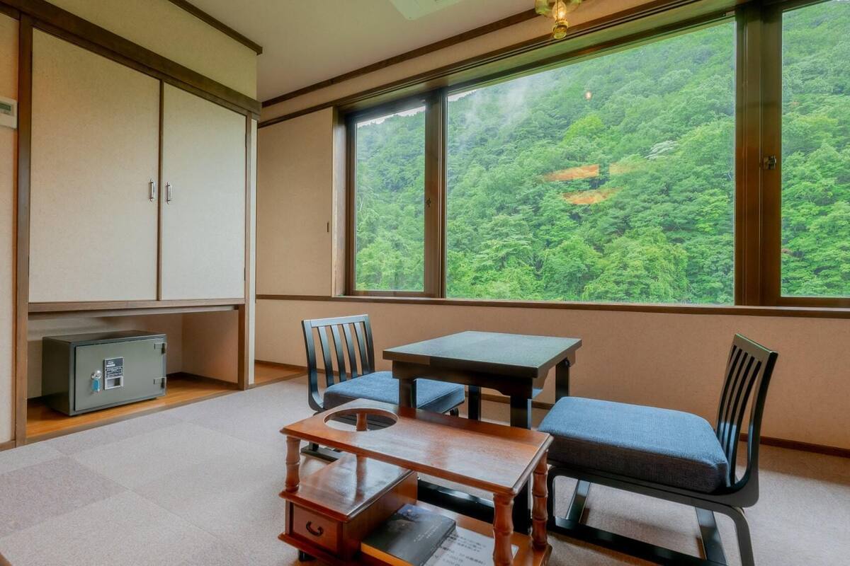Ein Zimmer mit Blick auf einen Wald, ein kleiner Tisch, zwei Stühle, ein Schrank und ein Safe.