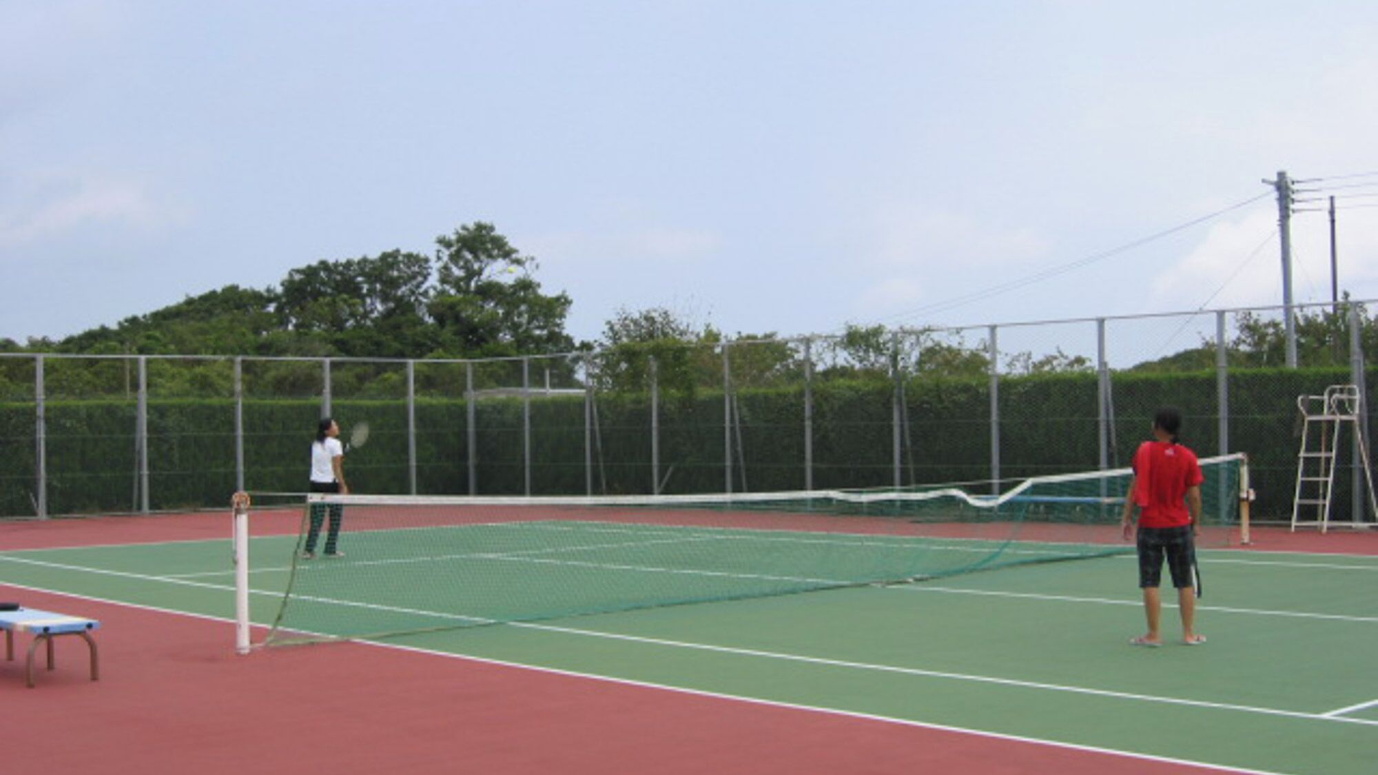 A tennis court with a net, a fence, and a ladder.
