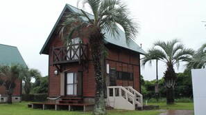 A wooden cabin with a balcony and stairs leading to the entrance. - Sansan Tomie Camping Village <goto Fukue> (Goto)