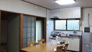 Eine kleine Küche mit Esstisch, Stühlen, Mikrowelle, Kühlschrank und einem Fenster mit Jalousien.