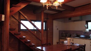 Eine Holztreppe führt zu einem Essbereich mit Tisch und Stühlen, im Hintergrund ist eine Küche zu sehen, und eine Chandelüster erleuchtet den Raum.