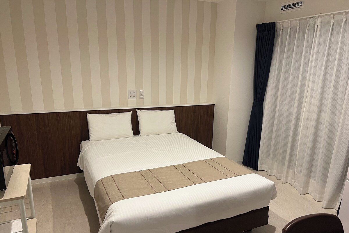 A hotel room with a large bed, a wooden headboard, a bedside table, and a chair.