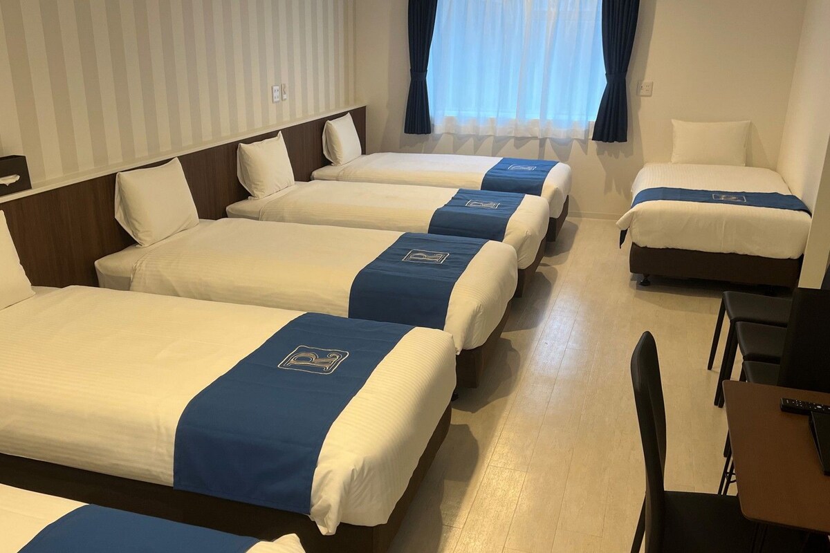 A hotel room with four beds arranged in a row, each with a blue headboard and white bedding.