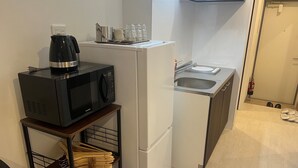 Et lille tekøkken med en sort mikrobølgeovn, et hvidt køleskab, en vask og en kaffemaskine på en hylde.