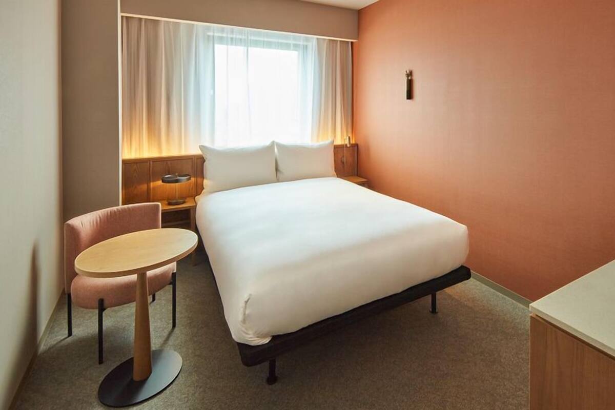 Een hotelkamer met een bed, een bureau, een stoel, een nachtkastje en een raam met gordijnen.