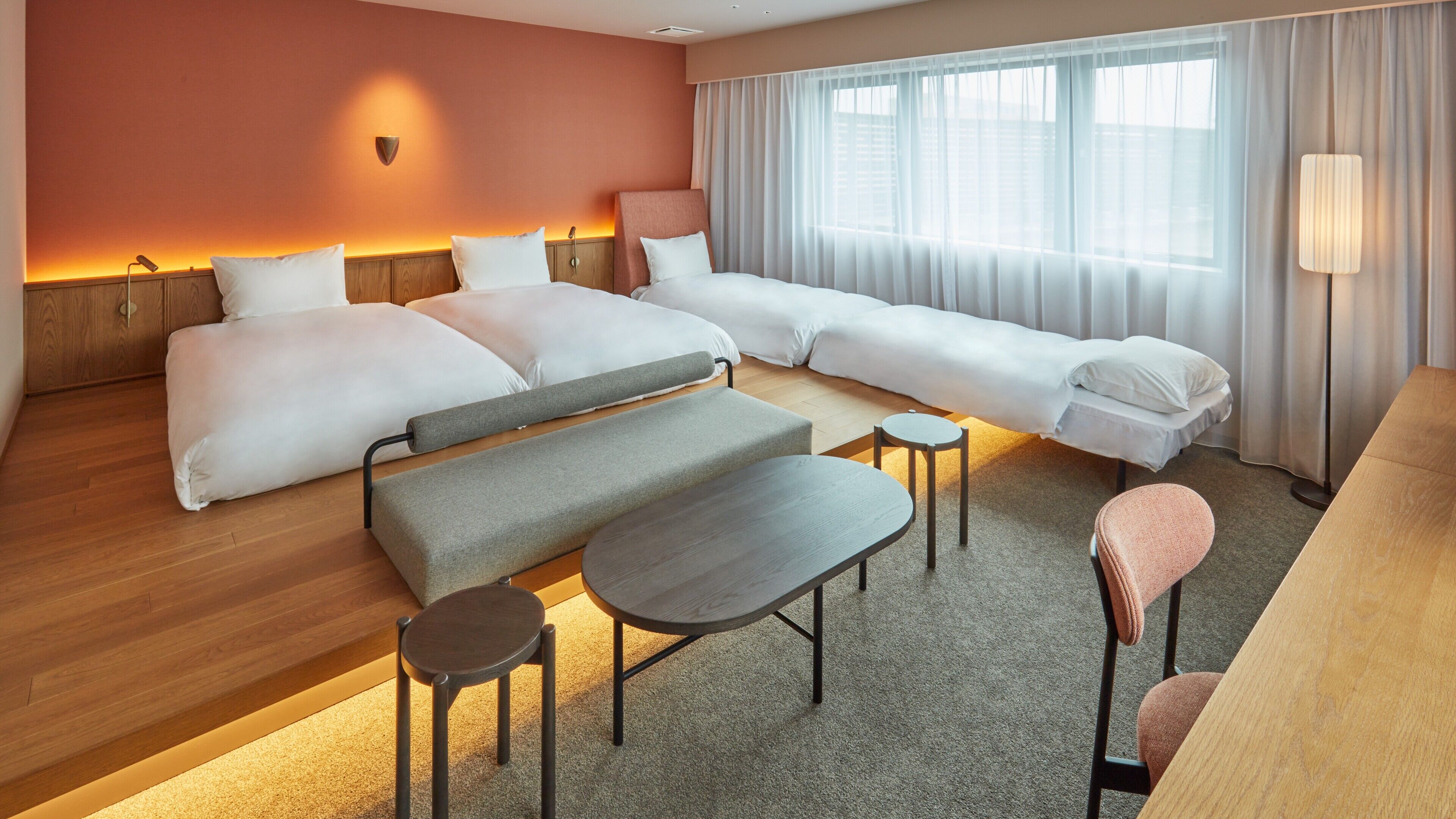 Une chambre d’hôtel avec deux lits, un canapé, une petite table, un banc et une lampe.
